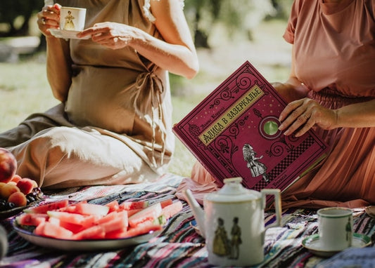 Дві жінки на пікніку з чаєм, кавуном і книгою «Аліса в Задзеркаллі»