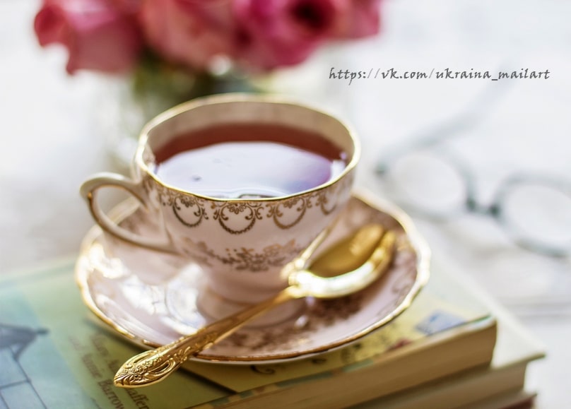 Vintage-Teetasse mit goldenem Löffel auf einem Bücherstapel, im Hintergrund Brille und Rosen