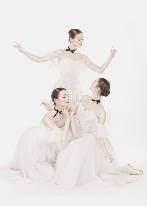 Drei Ballerinas in weißen Tutus und schwarzen Bändchen posieren gemeinsam