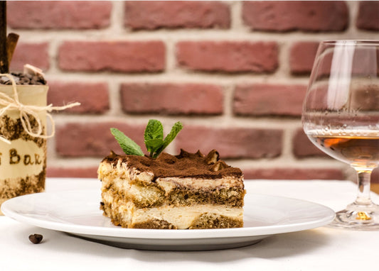 Stück Tiramisu mit Minze und Kakao auf einem Teller neben einem Glas Kaffeelikör