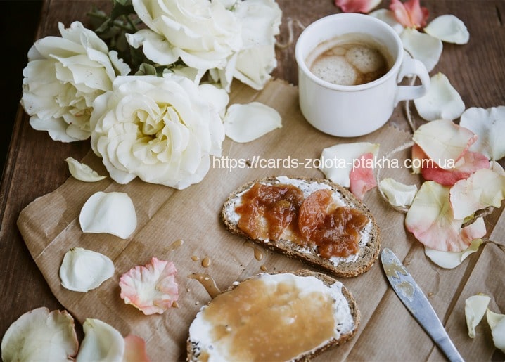 Toast mit Marmelade und Honig, Kaffeetasse und weiße Rosen auf einem Holztisch