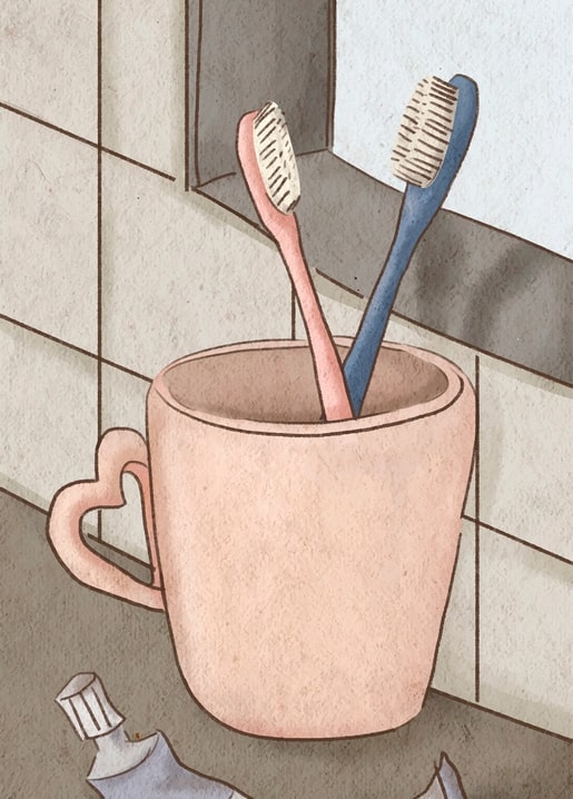 Rosa und blaue Zahnbürsten stecken in einer herzförmigen Tasse an der Badezimmerfliese