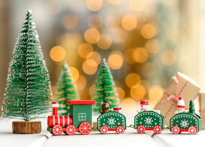 Wooden toy train with a teddy bear and gift passing miniature Christmas trees