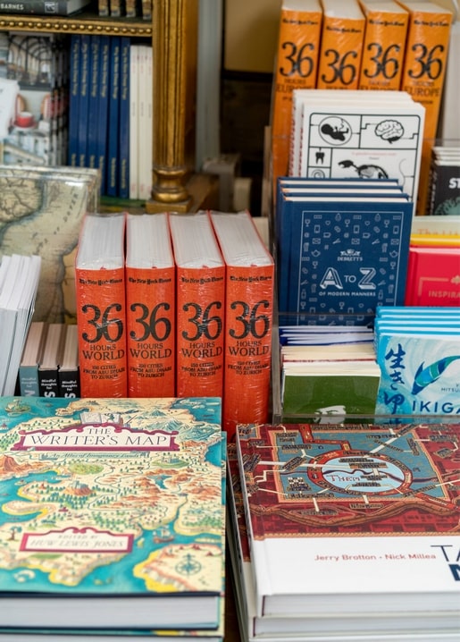 Стіл книгарні з оранжевими путівниками, книгами в обкладинках-мапах і розгорнутою картою