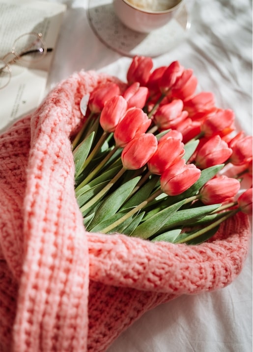 Coral tulip bouquet wrapped in a pink knitted blanket with coffee and a book