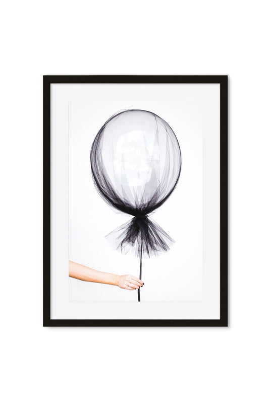 Black-and-white photo of a hand holding a balloon wrapped in sheer black tulle against a plain backdrop