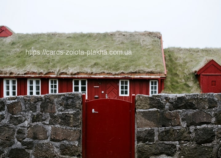 Rotes Holzhaus mit Grasdach hinter einer Steinmauer und rotem Gartentor
