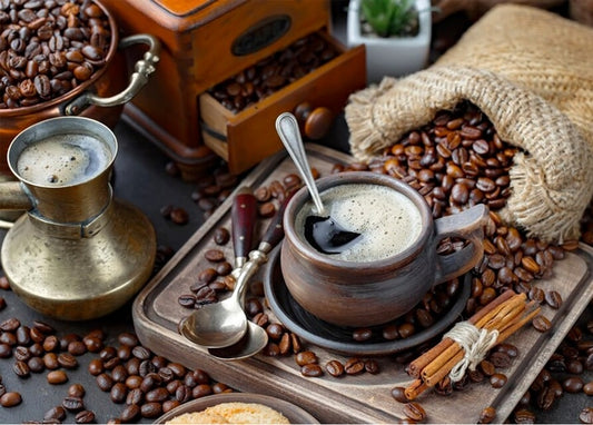 Kupferne Cezve und Tonschale mit Kaffee zwischen gerösteten Bohnen und einer alten Mühle