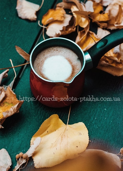 Copper Turkish coffee pot with frothy coffee on dark teal wood surrounded by autumn leaves