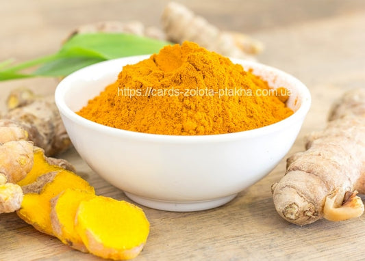 Bowl of golden ground turmeric beside fresh turmeric roots and a green leaf on a wood table