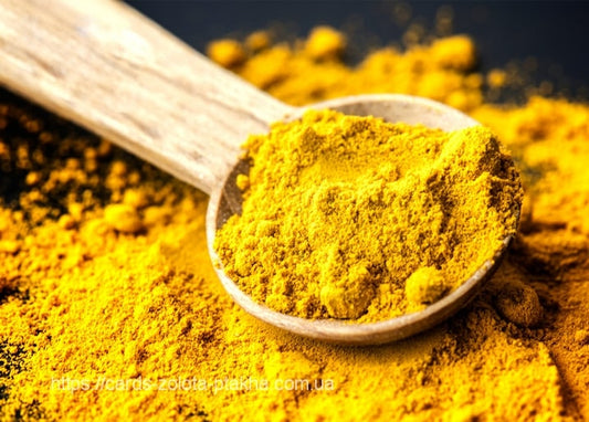 Heap of golden turmeric powder piled on a rustic wooden spoon, with more powder scattered around it