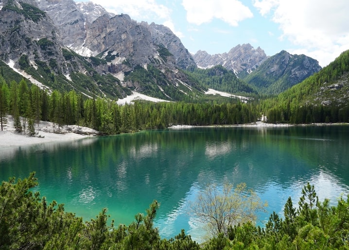 Türkisfarbener Alpensee, umgeben von Kiefernwald, unter zerklüfteten, schneebedeckten Gipfeln