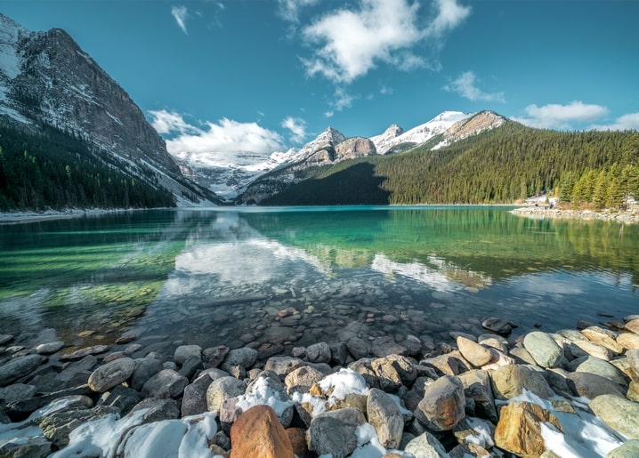 Türkiser Gletschersee mit schneebedeckten Bergen und steinigem Ufer