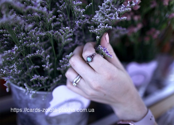 Hand mit Türkisring zwischen violetten Strandflieder-Blüten in einer Vase