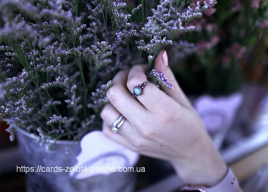 Hand mit Türkisring zwischen violetten Strandflieder-Blüten in einer Vase