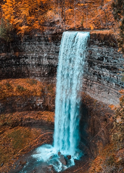 Turquoise waterfall cascading through a forest in blazing autumn orange