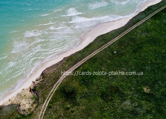 Aerial close-up of turquoise waves against a green cliff and dirt road, Bilhorod-Dnistrovskyi