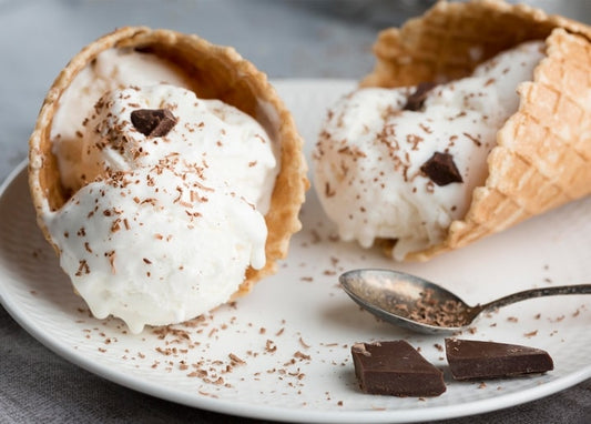 Zwei Waffelhörnchen mit Vanilleeis, Kakao und dunklen Schokoladenstückchen auf einem Teller