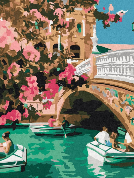 Stone arch bridge draped in pink bougainvillea, small boats crossing the turquoise water below
