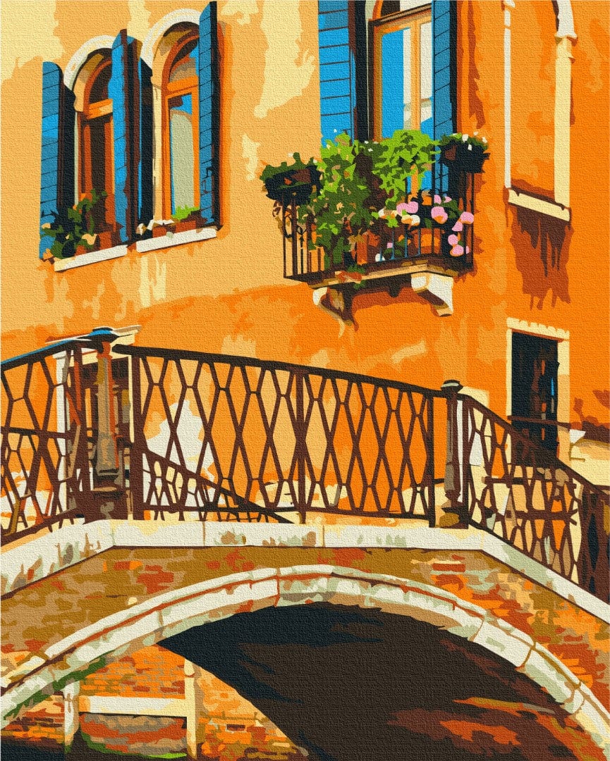 Venice canal scene with a stone bridge, iron railing, and a balcony overflowing with pink flowers