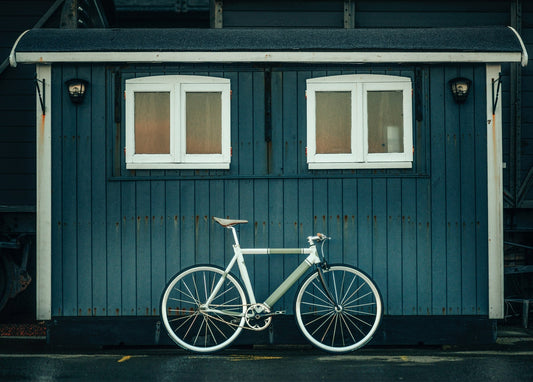 Cremefarbenes Vintage-Fahrrad lehnt an einem verwitterten blauen Holzschuppen mit weißen Fenstern