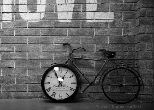 Black-and-white photo of a vintage bicycle with a decorative clock resting in its front wheel