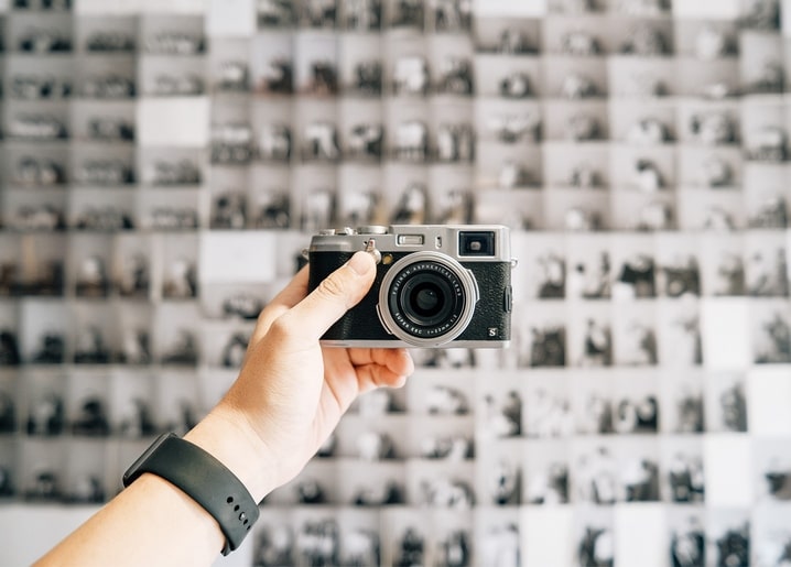 Hand hält eine Retro-Kamera vor einer Wand aus Schwarz-Weiß-Kontaktabzügen