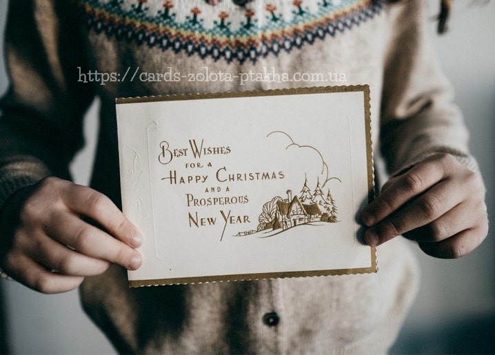 Goldgeprägte Vintage-Weihnachtskarte mit Häuschen-Motiv, in zwei Händen gehalten