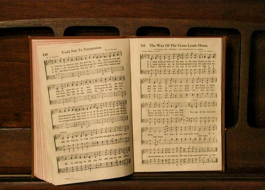 Aufgeschlagenes altes Gesangbuch mit vergilbten Notenseiten auf dunklem Holztisch.