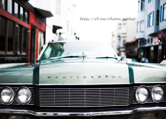 Nahaufnahme von Kühlergrill und Scheinwerfern eines mintgrünen Lincoln Continental auf einer Stadtstraße