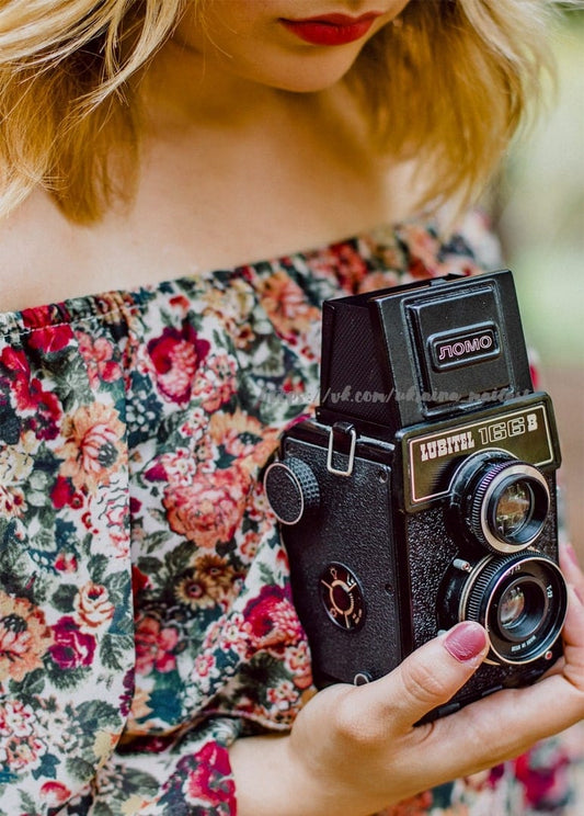 Дівчина у квітковій сукні тримає вінтажну камеру Lubitel 166B