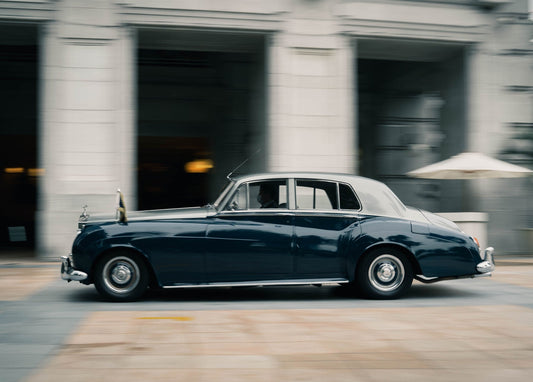 Dunkelblauer Rolls-Royce fährt an einer Steinkolonnade vorbei