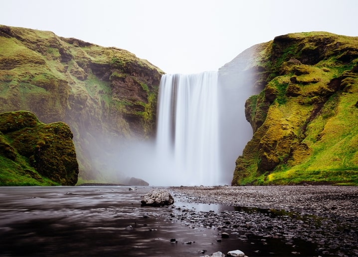 Wasserfall fällt durch Nebel in eine moosbewachsene grüne Schlucht