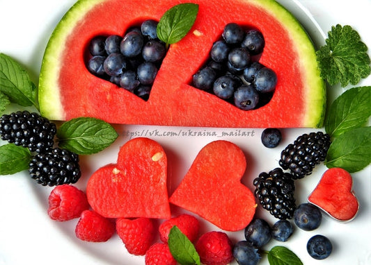 Wassermelonenscheiben und Heidelbeeren in Herzform, umgeben von Brombeeren und Himbeeren