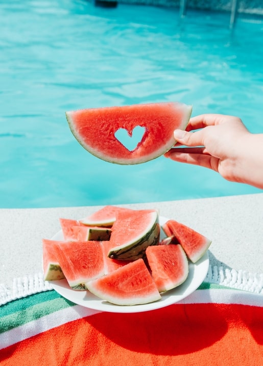 Herzförmige Wassermelonenscheibe über einem Teller mit Melonenstücken am Pool
