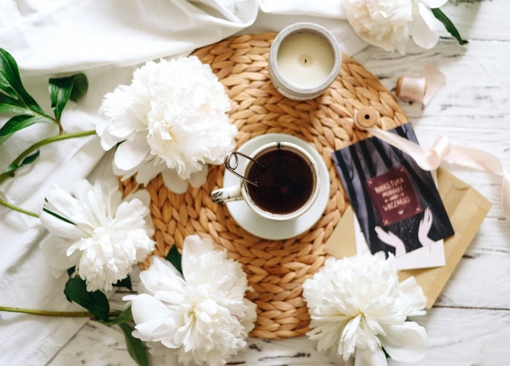 Weiße Pfingstrosen um eine Tasse Kaffee, eine brennende Kerze und eine Geschenkkarte mit Schleife