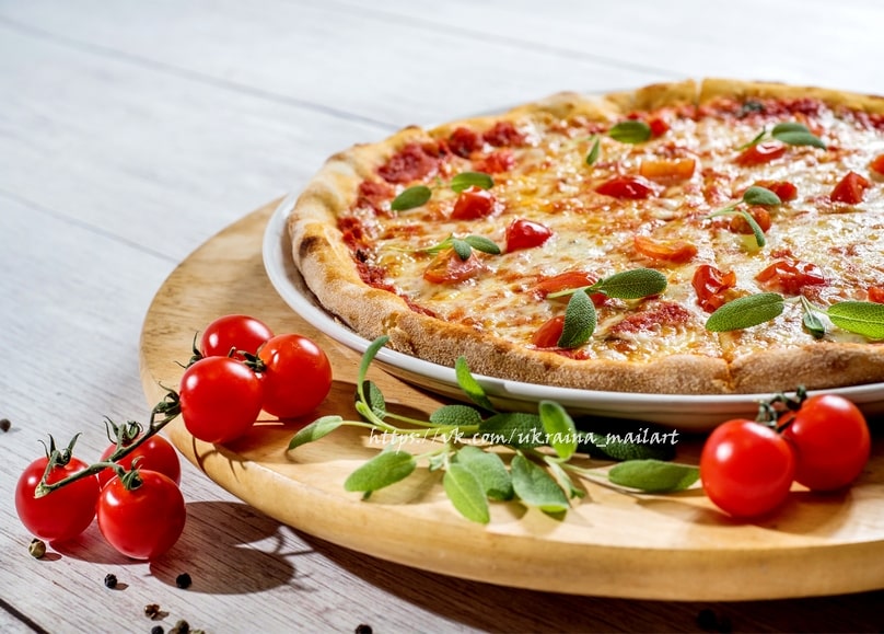 Whole baked pizza on a wooden board with cherry tomatoes on the vine