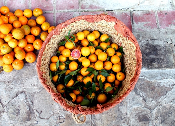 Weidenkorb mit Orangen und aufgeschnittener Blutorange auf Steinboden