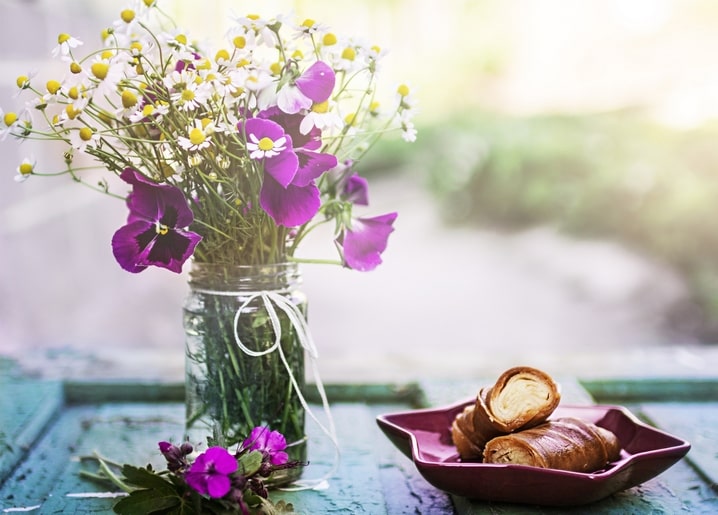 Wildblumen im Einmachglas neben einem Teller mit Gebäckröllchen auf türkisfarbenem Tisch