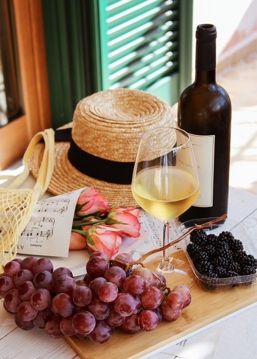 Weißwein, Strohhut, Rosen, Trauben und Brombeeren vor grünen Fensterläden
