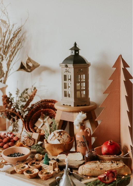 Rustic winter flat-lay with a lantern, wooden toy train, bread, cheese and pomegranates on a wooden table
