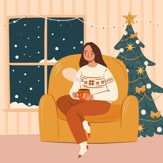 Woman in a Nordic sweater drinking tea in an armchair beside a decorated Christmas tree and snowy window