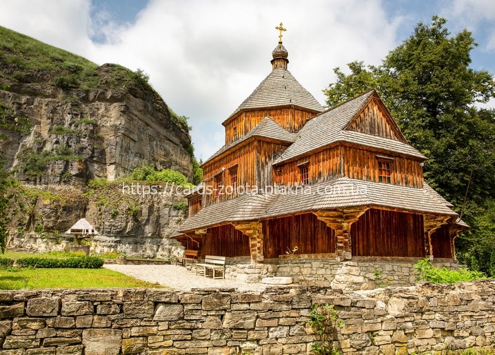 Hölzerne Kirche mit Schindeldach neben einer schroffen Felsklippe in der Ukraine