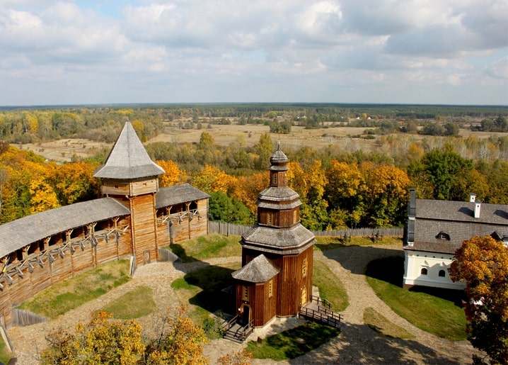 Дерев'яна фортечна стіна та церква з ґонтовим куполом серед осіннього лісу з висоти