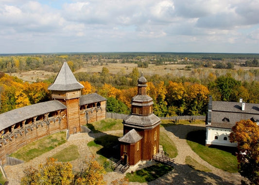Aerial view of a wooden fortress wall and shingle-domed church surrounded by autumn trees