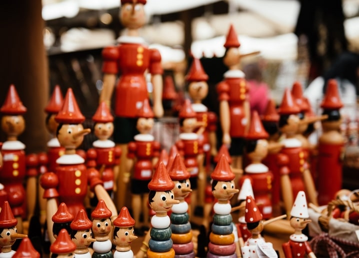 Wooden Pinocchio dolls with red pointed caps lined up at a market stall