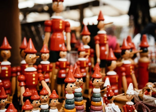 Wooden Pinocchio dolls with red pointed caps lined up at a market stall