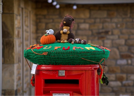 Roter britischer Postbox mit gehäkelter grüner Herbstmütze, Kürbis, Igel und Eicheln
