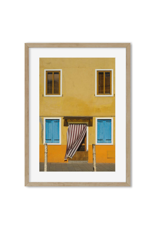 Yellow house facade with blue and brown shutters and a striped curtain in the doorway