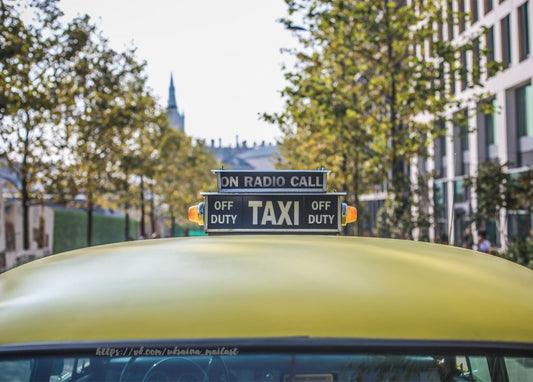 Gelbes Taxi mit Dachschild „TAXI“ auf einer baumgesäumten Straße